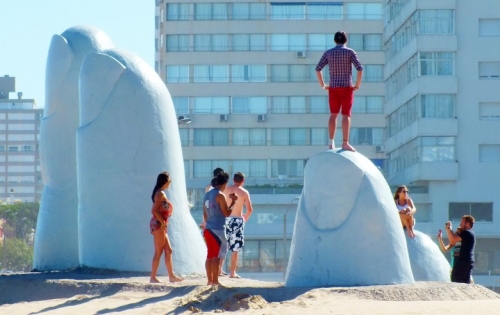 Un hombre parado sobre uno de los dedos de la escultura ubicada en la Brava de Punta del Este
