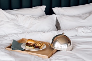 Bandeja de servicio de habitaciones con una hamburguesa y patatas fritas encima de una cama de hotel. 